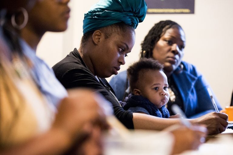 Thaashae Reingoud (center) takes notes as her son, Amir, sits on her lap at the 