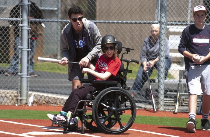 Devon Reed takes her turn at bat helped by Baily Otto, a volunteer from Stockton University, during opening day at the South Jersey Field of Dreams in Absecon N.J. (Anthony Smedile for WHYY)