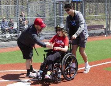 Rob Reed congratulates Devon Reed as she crosses home plate with help from Baily Otto, a volunteer from Stockton University, during opening day at The South Jersey Field of Dreams in Absecon, New Jersey. The Field of Dreams is a place where physically and mentally disabled children and adults can participate in the game of baseball. (Anthony Smedile for WHYY)