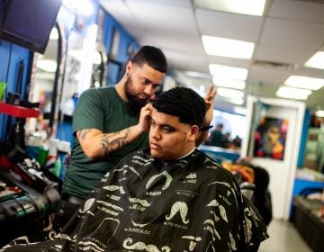 Bryan Romero has his hair cut by barber Jojo at Vibes barber shop on fifth street in the Fairhill section of Philadelphia. (Brad Larrison for WHYY)