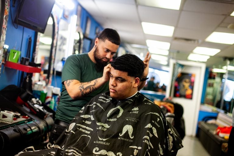 Bryan Romero has his hair cut by barber Jojo at Vibes barber shop on fifth street in the Fairhill section of Philadelphia. (Brad Larrison for WHYY)