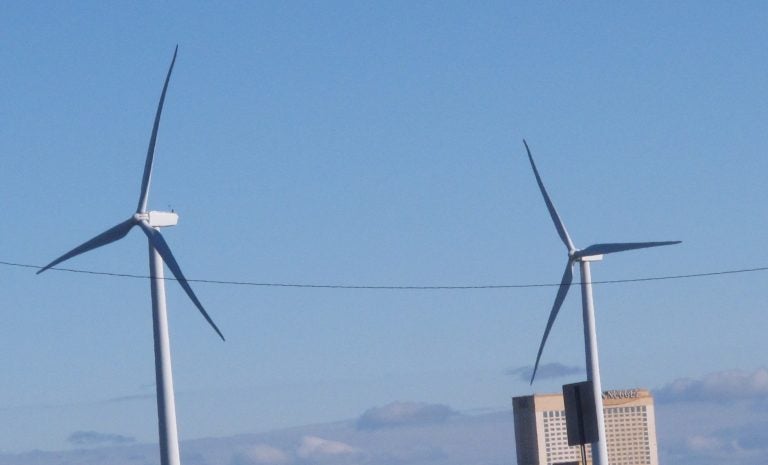 Windmills turn agains the backdrop of a blue sky.