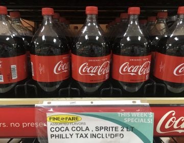 A sweetened beverage tax sign is seen below a row of Coca Cola bottles