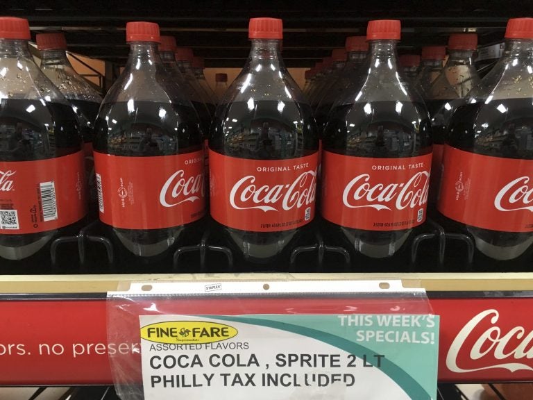 A sweetened beverage tax sign is seen below a row of Coca Cola bottles