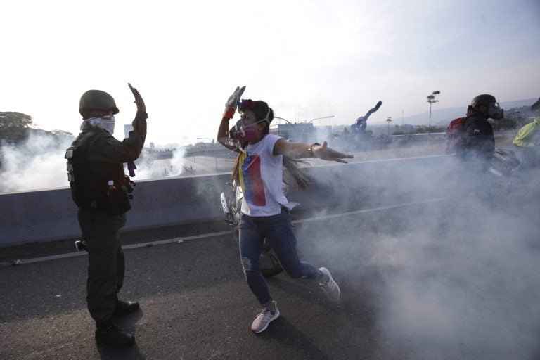 An opponent to Venezuela's President Nicolas Maduro high fives a rebel soldier on a highway overpass outside La Carlota air base amid tear gas fired by loyalist soldiers inside the base in Caracas, Venezuela, Tuesday, April 30, 2019. Venezuelan opposition leader Juan Guaidó took to the streets in Caracas with activist Leopoldo Lopez and a small contingent of heavily armed troops early Tuesday in a bold and risky call for the military to rise up and oust socialist leader Nicolas Maduro. (Boris Vergara/AP Photo)