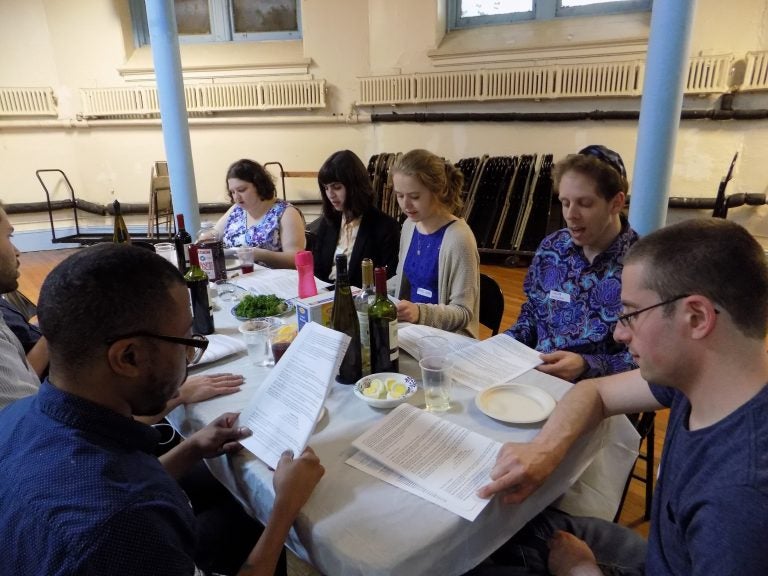 People attending the LGBTQ Seder read from the Haggadah modified by host Galia Godel to celebrate the queer Jewish experience. (Ximena Conde/WHYY)