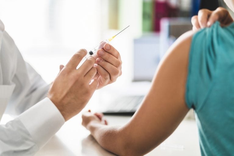 A doctor holds a vaccine syringe close to a patients exposed arm.