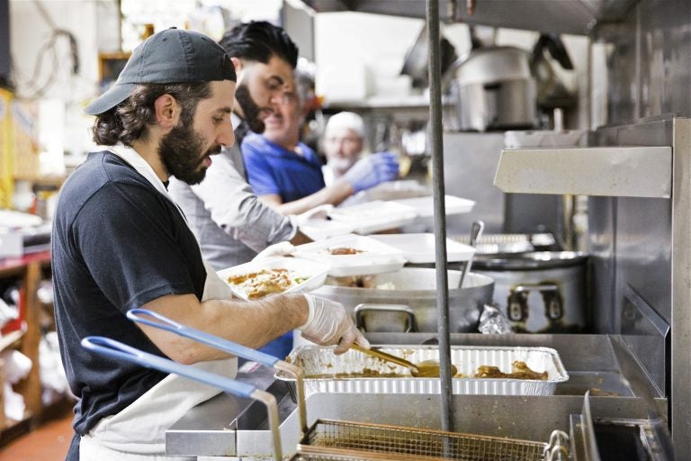 (From left) Anas Dabbour, Abbulah Ibrahim, and Munir Odeh work in an assembly line to create boxes of fish, chicken, and lamb dinners at the Al Amana Grocery on May 20, 2019. Dabbour's family established the grocery in 1993, after emigrating from Syria in 1992. (Rachel Wisniewski for WHYY)