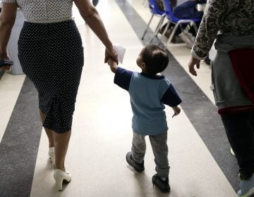 In this Friday, Jan. 11, 2019, photo, Maria Orbelina Cortez, (right), walks with her 3-year-old son, Julio, (center), and a worker at the Catholic Charities shelter in McAllen, Texas. Orbelina says she decided to flee El Salvador after her husband attacked her and caused a pan of hot oil to fall, scalding Julio and leaving a scar on his head. (Eric Gay/AP Photo)