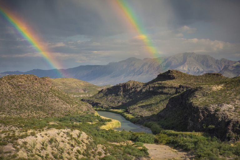 This December, 2017 photo released by Fin and Fur Films shows a double rainbow over Big Bend National Park, Texas, and the Rio Grande along the U.S.-Mexico border, with Mexico being on the right side of the river. The new documentary, 