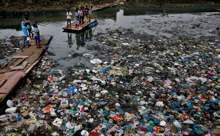 In this Sunday, Oct. 2, 2016 file photo, a man guides a raft through a polluted canal littered with plastic bags and other garbage in Mumbai, India. United Nations officials say nearly all of the world's countries have agreed on a deal to better manage plastic waste, with the United States a notable exception. A 