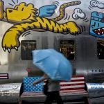 A woman walks by a bench painted with an American flag outside a fashion boutique selling U.S. brand clothing at the capital city's popular shopping mall in Beijing, Monday, May 13, 2019.  Companies waited Monday to see how China decides to retaliate for President Donald Trump’s latest tariff hike while forecasters warned their escalating fight over technology and trade might disrupt a Chinese economic recovery. (Andy Wong/AP Photo)