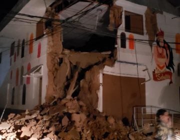 In this photo provided by Firefighters of Peru, people pass in front destroyed wall in Yurimaguas Peru, Sunday, May 26, 2019. A powerful magnitude 8.0 earthquake struck the Amazon jungle in north-central Peru early Sunday, the U.S. Geological survey reported, collapsing buildings and knocking out power to some areas. (Firefighters of Peru via AP)