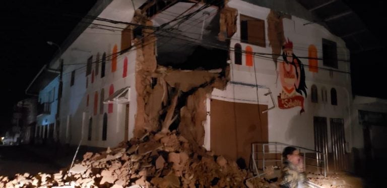 In this photo provided by Firefighters of Peru, people pass in front destroyed wall in Yurimaguas Peru, Sunday, May 26, 2019. A powerful magnitude 8.0 earthquake struck the Amazon jungle in north-central Peru early Sunday, the U.S. Geological survey reported, collapsing buildings and knocking out power to some areas. (Firefighters of Peru via AP)