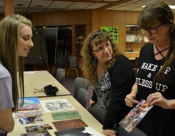 Mt. Aloysius College student Kylee Clawson, at left, and Pamela Townsend, center, look at art made by Jenny Behe, at right. Clawson, a surgical technology major, is participating in the art program as part of a college class. Townsend and Behe each have struggled with behavioral illnesses and work as peer support specialists. (Brett Sholtis/Transforming Health) 