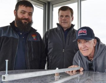 Officials from the Moshannon Forest District gather around the alidade, an instrument used to help personnel staffing lookout towers pinpoint the location of wildfires. From left to right, Joe Polaski, John Hecker and Larry Bickel stand in the new Chestnut Ridge tower. (Amy Sisk / StateImpact Pennsylvania)