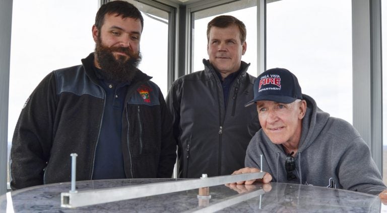 Officials from the Moshannon Forest District gather around the alidade, an instrument used to help personnel staffing lookout towers pinpoint the location of wildfires. From left to right, Joe Polaski, John Hecker and Larry Bickel stand in the new Chestnut Ridge tower. (Amy Sisk / StateImpact Pennsylvania)