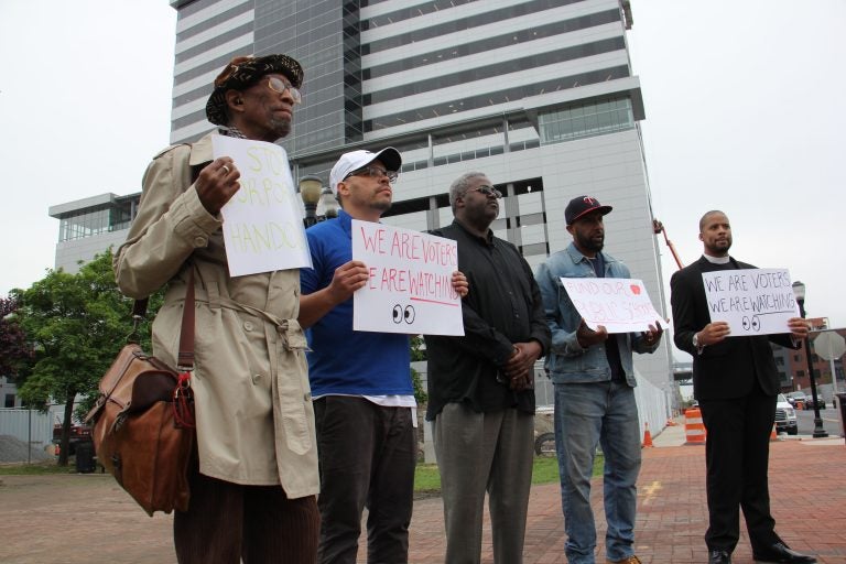 A small group of protesters gather outside Camden’s newest corporate high rise, demanding that beneficiaries of state tax breaks demonstrate what they’re doing to help Camden residents. (Emma Lee/WHYY)