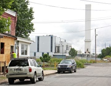 The smokestack of the Delaware Valley Resource Recovery Facility looms over a residential street in Chester. (Emma Lee/WHYY)