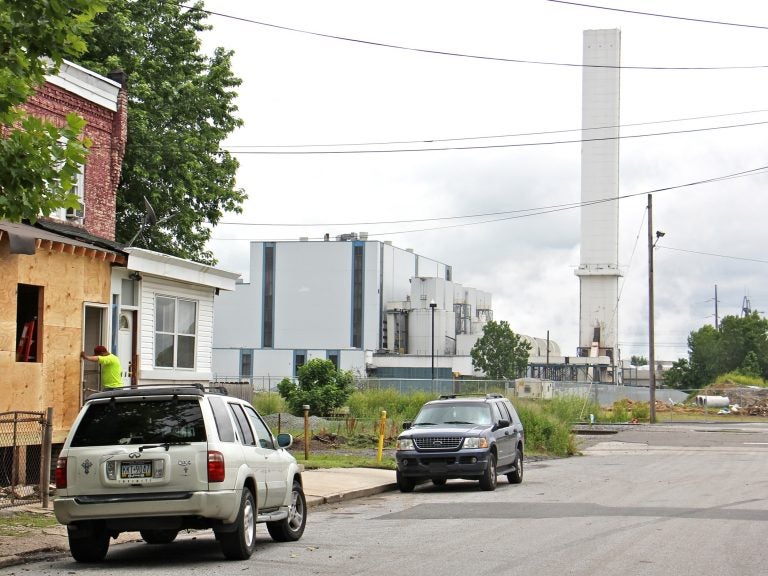 The smokestack of the Delaware Valley Resource Recovery Facility looms over a residential street in Chester. (Emma Lee/WHYY)
