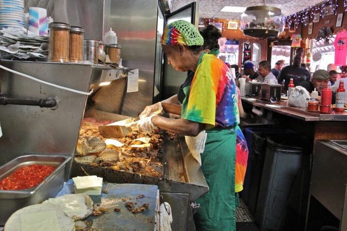A fry cook tends to meat and onions sizzling on the griddle at Donkey's Place in Camden. (Emma Lee/WHYY)