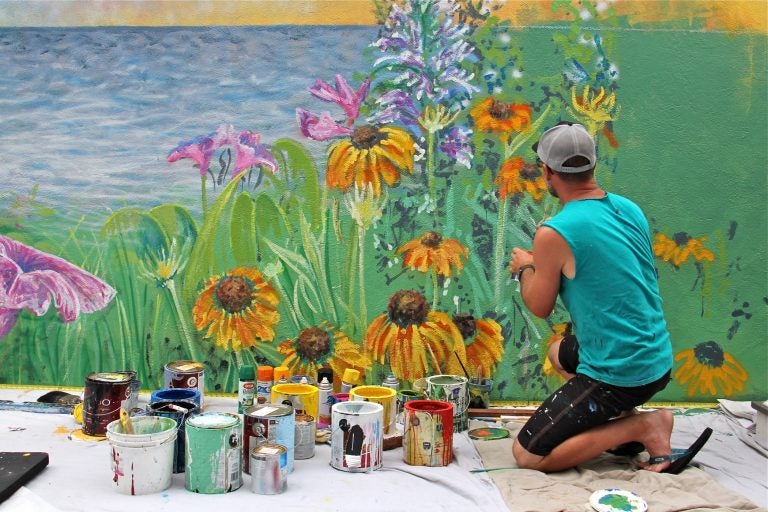 Philadelphia artist Charles Barbin covers a cinderblock wall with a seascape mural at the home of Rose Ann Cahill in Ventnor. The bayside home was raised 8 feet after it was damaged by Superstorm Sandy. (Emma Lee/WHYY)