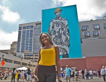 Najee Spencer-Young poses in front of her mural portrait by artist Amy Sherald. Spencer-Young is a participant in the Mural Arts’ Achieving Independence Center classes. (Kimberly Paynter/WHYY)
