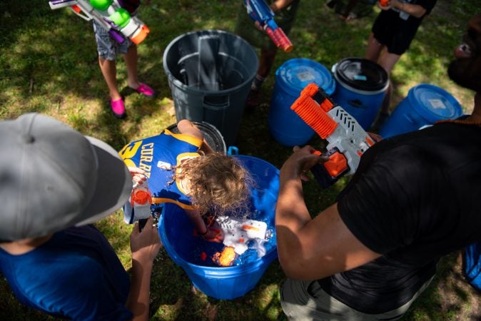 Participants in Water Fight Philly refiill their water guns from barrels on Sunday, June 30, 2019. (Kriston Jae Bethel for WHYY)