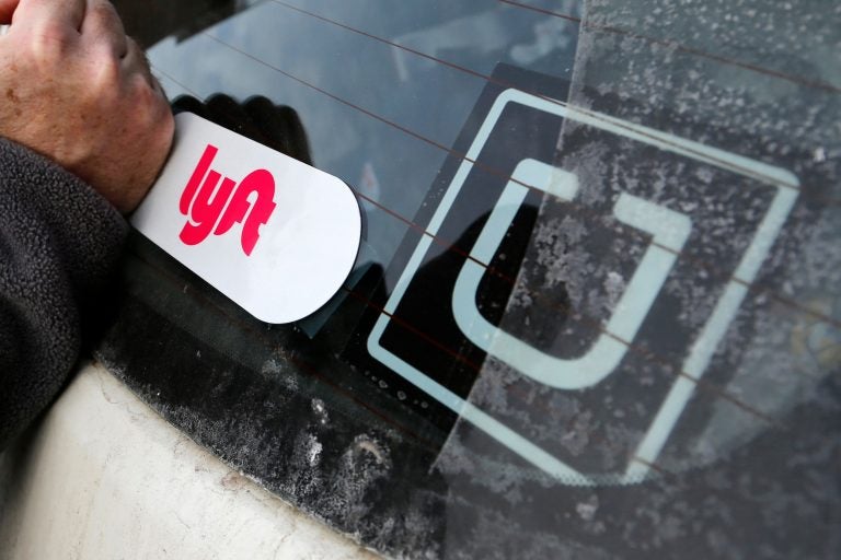 A Lyft logo is installed on a Lyft driver's car next to an Uber sticker