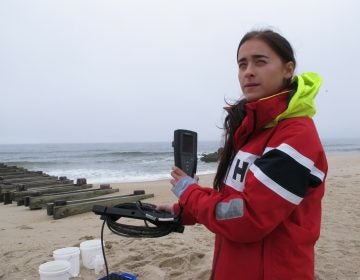 This May 30, 2019 photo shows Skye Post, who will be a junior at Monmouth University this fall, demonstrating water quality testing equipment near a storm drain outfall pipe on the beach in Long Branch, N.J. University researchers are studying the relationship between heavy rainfall and elevated levels of bacteria from animal waste that gets flushed into storm sewers and out in the ocean at popular surfing beaches at the Jersey shore. (Wayne Parry/AP Photo)