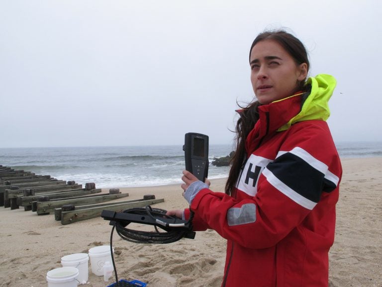 This May 30, 2019 photo shows Skye Post, who will be a junior at Monmouth University this fall, demonstrating water quality testing equipment near a storm drain outfall pipe on the beach in Long Branch, N.J. University researchers are studying the relationship between heavy rainfall and elevated levels of bacteria from animal waste that gets flushed into storm sewers and out in the ocean at popular surfing beaches at the Jersey shore. (Wayne Parry/AP Photo)