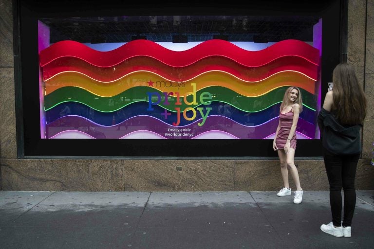 In this Wednesday, June 19, 2019, photo, a visitor to Herald Square takes a photo with the Pride and Joy window display at the Macy's flagship store in New York. For Pride month, retailers across the country are selling goods and services celebrating LGBTQ culture. Macy’s flagship store is adorned with rainbow-colored Pride tribute windows, set in the same space as its famous Christmas displays. (Mary Altaffer/AP Photo)