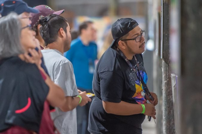 Alexander DeLeon takes a close up inspection of one of the artworks. DeLeon, a Trenton-based artist, had one of his pieces featured in the exhibit. (Jonathan Wilson for WHYY)