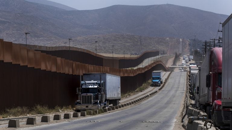 Trucks pass along a border wall as they get into position to cross into the United States at the border in Tijuana, Mexico, on Friday. Companies have been rushing to ship as many goods as possible out of Mexico to get ahead of possible tariffs threatened by President Donald Trump, hurriedly sending cars, appliances and construction materials across the border to beat Monday's deadline. (Hans-Maximo Musielik/AP)