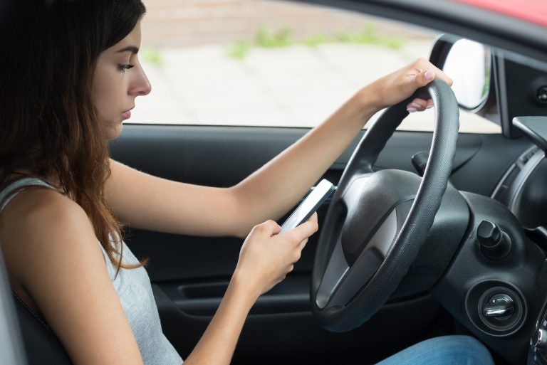 Side View Of Young Woman Using Mobile Phone While Driving Car