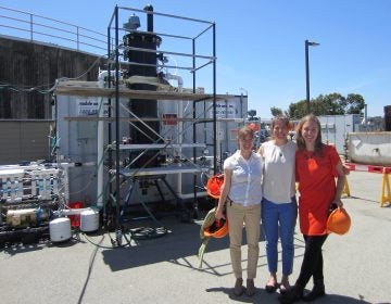 Anne Schauer-Gimenez (from left) Allison Pieja and Molly Morse of Mango Materials stand next to the biopolymer fermenter at a sewage treatment plant next to San Francisco Bay. The fermenter feeds bacteria the methane they need to produce a biological form of plastic. (Chris Joyce/NPR)