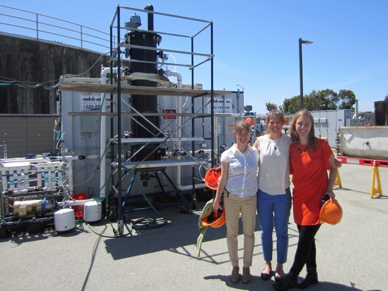 Anne Schauer-Gimenez (from left) Allison Pieja and Molly Morse of Mango Materials stand next to the biopolymer fermenter at a sewage treatment plant next to San Francisco Bay. The fermenter feeds bacteria the methane they need to produce a biological form of plastic. (Chris Joyce/NPR)