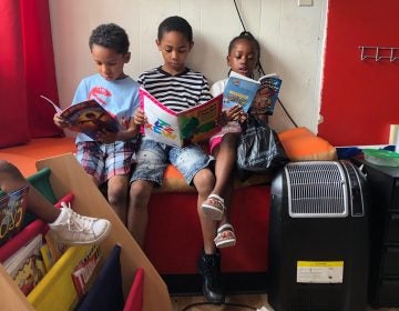 Christian Howell (center) is flanked by younger siblings Kaiden and Karima at the African Barbershop on North Market Street in Wilmington. (Cris Barrish/WHYY)