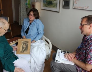 Thor Ringler (right) interviewed Ray Miller (left) in Miller's hospital room at the William S. Middleton Memorial Veterans Hospital in Madison, Wis., in April. Miller's daughter Barbara (center) brought in photos and a press clipping from Miller's time in the National Guard to help facilitate the conversation. (Bram Sable-Smith for NPR)