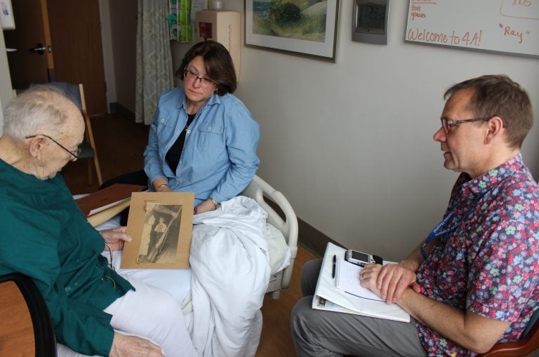 Thor Ringler (right) interviewed Ray Miller (left) in Miller's hospital room at the William S. Middleton Memorial Veterans Hospital in Madison, Wis., in April. Miller's daughter Barbara (center) brought in photos and a press clipping from Miller's time in the National Guard to help facilitate the conversation. (Bram Sable-Smith for NPR)