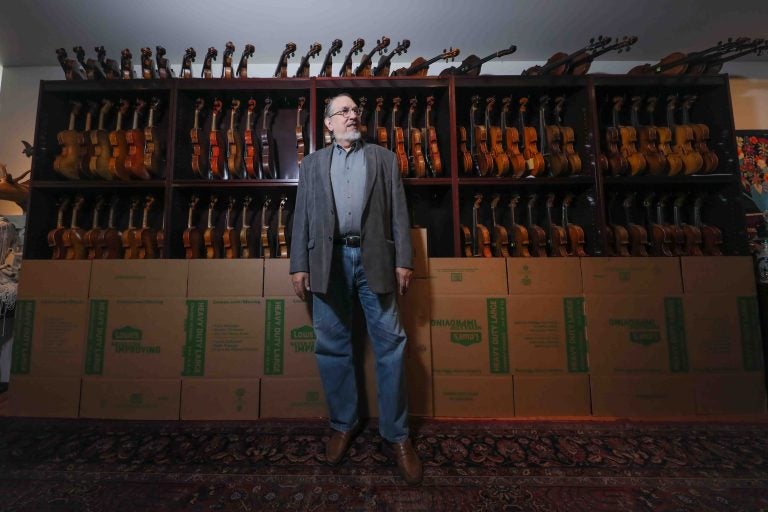 Singer-songwriter and session musician David Bromberg stands in front of a portion of his collection of violins. (Saquan Stimpson for WHYY)