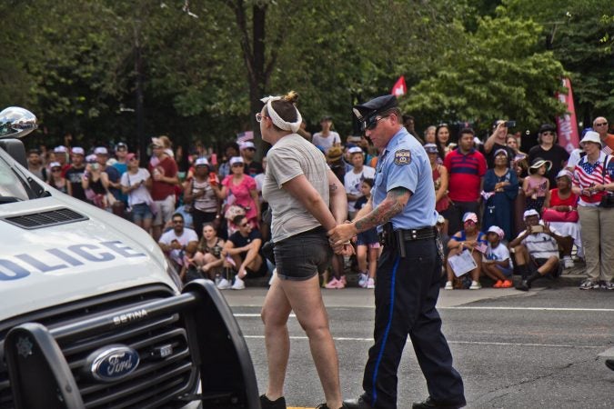 A protester demanding immigrants at the border be removed from detention centers is arrested at Philadelphia’s Fourth of July Parade. (Kimberly Paynter/WHYY)