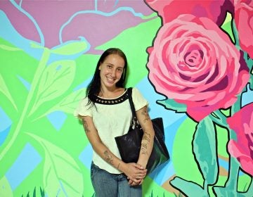 Becky Green, 27, stands in front of the mural she helped to create in SEPTA Suburban Station. (Emma Lee/WHYY)