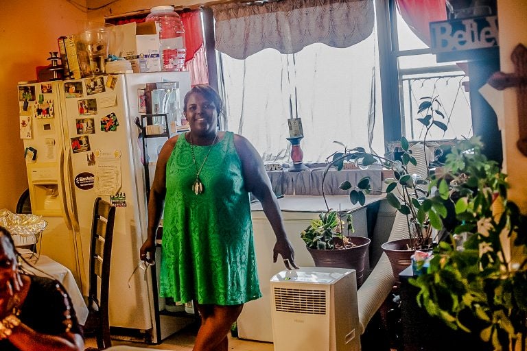 Sheila Armstrong stands in the living room of her 13th floor apartment at the Harrison Plaza buidling at 1050 North 10th Street where she installed an A/C unit to deal with the summer heat. (Brad Larrison for WHYY)