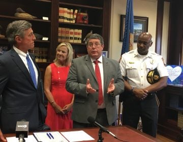 Smyrna School District Superintendent Patrick Williams (third from left)talks about legislation allowing police to inform school leaders when a student experiences a traumatic event. (From left) Gov. John Carney, Lt. Gov. Bethany Hall-Long, and Smryna Police Chief Torrie James stand alongside Williams in Carney’s Dover office. (Mark Eichmann/WHYY)