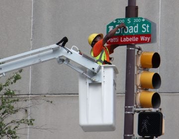 A worker bolts on a sign changing a block of Broad Street Patti LaBelle Way. (Emma Lee/WHYY)