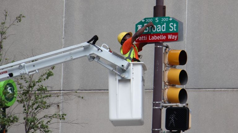 A worker bolts on a sign changing a block of Broad Street Patti LaBelle Way. (Emma Lee/WHYY)