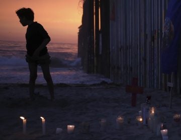 A youth stands Sunday by the border fence that separates Mexico from the U.S., where candles and crosses stand in memory of the father and daughter who died during their journey toward the U.S. (Emilio Espejel/AP)