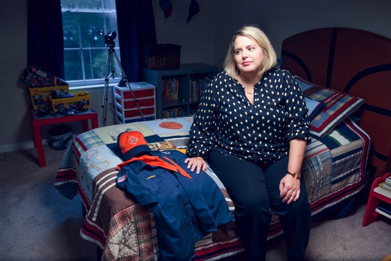 Leslie Slingsby, executive director of Mission Kids, sits on her sons bed with his Boy Scouts of America uniform and handbook at her Collegeville, Pa. home on August 14, 2019. Slingsby's nonprofit works on behalf of Montgomery County to investigate claims of child abuse and advocates for child protection around the world. (Kriston Jae Bethel for WHYY)