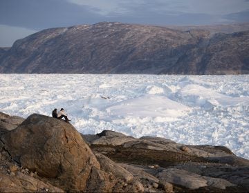 In this Aug. 16, 2019, photo, New York University student researchers sit on a rock overlooking the Helheim glacier in Greenland.  U.S. President Trump announced his decision to postpone an early September visit to Denmark by tweet Tuesday Aug. 20, 2019, after Danish Prime Minister Mette Frederiksen dismissed the notion of selling Greenland to the U.S. as 